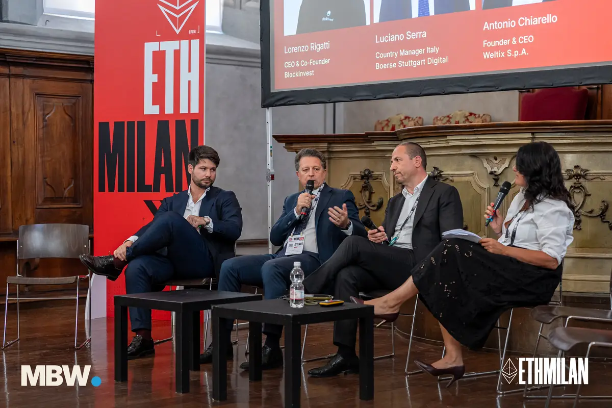 A panel of four on the ETHMilan stage, one speaker holding the microphone